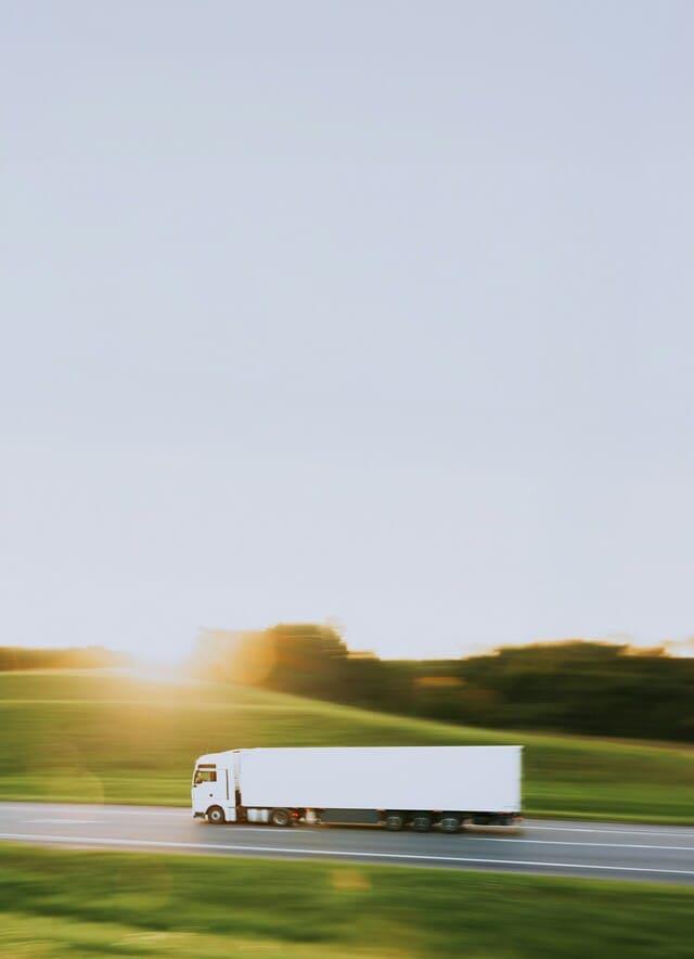 Un camion blanc roule sur une route avec un coucher de soleil en arrière-plan.